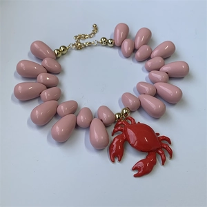Detail of beaded necklace with red crab pendant, pink teardrop beads, and gold metal accents