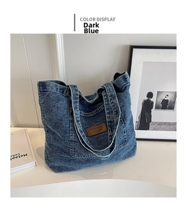 Detail of dark blue washed denim tote bag with brown leather tag on a white surface