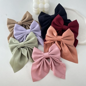 Close-up of seven assorted colorful bow hair clips in satin fabric on white tray