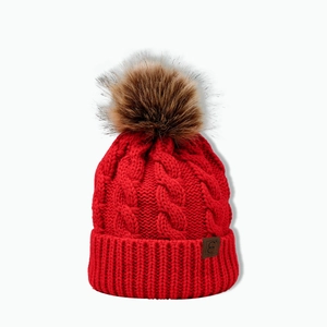 Detail of red cable knit beanie featuring a brown faux fur pom and leather logo patch