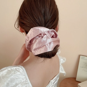Detailed view of an oversized pink satin scrunchie with soft pleats and elegant silk texture