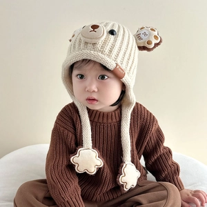 Detail of baby bear knitted hat with cute paw print chin straps and fur ear decor