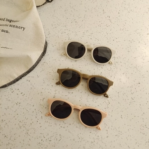Detailed flat lay of three retro round baby sunglasses in cream, olive, and dusty pink shades