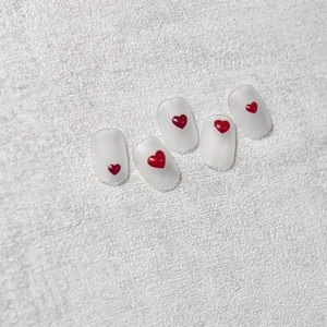 Detail of translucent matte press-on nails with 3D red heart charms on white background