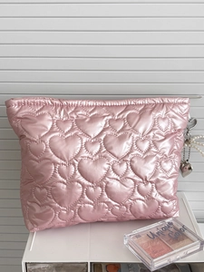 Pink heart quilted satin makeup bag with heart pearl charm on a minimalist storage rack