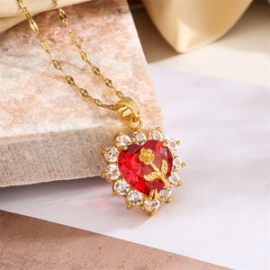 Close-up of heart-shaped gold necklace with red gemstone and rose detail on stone base
