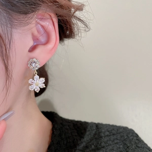 Close-up of golden flower drop earrings with inlaid zircons worn by a female model