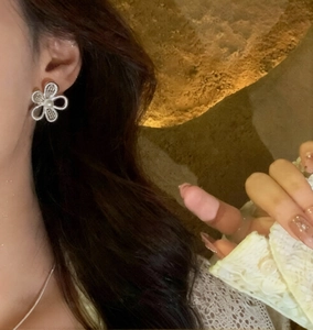 Detail view of hollow flower earrings with white pearl center worn on earlobe