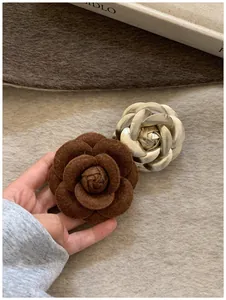 Detailed view of layered camellia brooches in dark brown felt and gold metallic finish