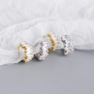 Macro view of gold and silver rectangular zircon earrings on soft white fabric