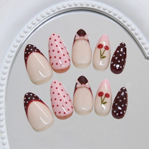 Pink and brown press-on nails with cherry patterns and 3D bow accents in almond shape