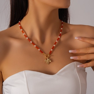 Detail of red and white beaded necklace with golden maple leaf pendant and toggle clasp