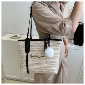Straw woven tote bag detail showing black handles and Suemmr embroidery with pompom