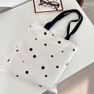 Minimalist polka dot canvas tote bag with black straps and glasses on a desk