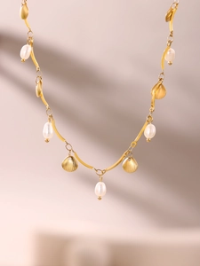 Detail of golden shell charms and irregular freshwater pearls on a stainless steel necklace