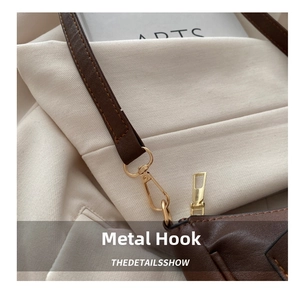 Detail shot of the golden metal hook and smooth zipper on a brown leather crescent bag