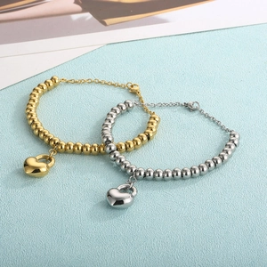 Close-up of gold and silver beaded bracelets featuring heart lock charms on textured background