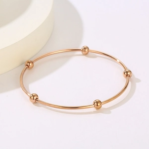 Detailed shot of a minimalist rose gold bangle with five movable metal beads on white background