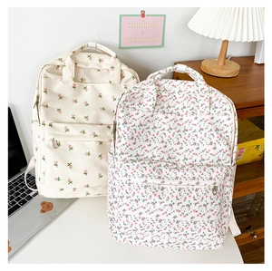 Detailed view of floral canvas backpacks on a desk with a laptop in a school setting