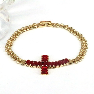 Detail of gold chain bracelet with cross pendant inlaid with red cubic zirconia
