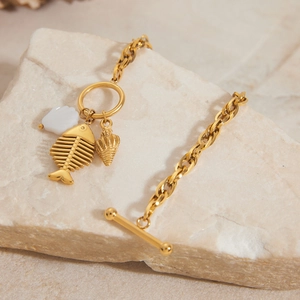 Détail des breloques arête de poisson et coquillage sur un bracelet doré à fermoir OT