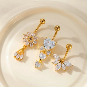 Détail de trois piercings de nombril dorés avec pendentifs en zircon fleur, cœur et feuille