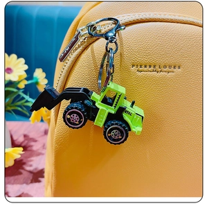 Green mini excavator keychain with silver metal ring hanging on a yellow textured backpack