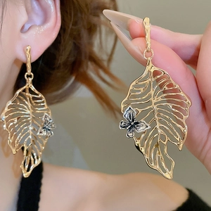 Detail of hollow leaf earrings with silver butterfly relief in gold-tone metal finish