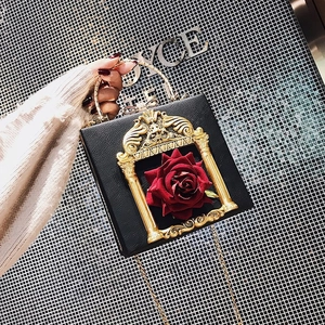 Detail of a black box bag featuring a 3D red rose inside a gold baroque relief frame