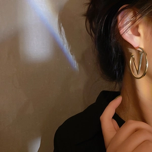 Detailed close-up of golden circular earring featuring a stylish V logo design