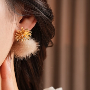 Close-up of model wearing gold firework floral stud earrings with beige pompom detail