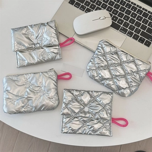 Silver quilted metallic makeup pouches in various sizes with pink hand straps on white desk