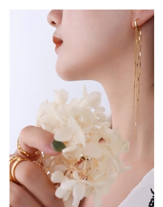 Detailed view of long gold tassel earrings and layered rings on a fashion model