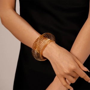 Close-up of a wide hollow spiral gold metal cuff bracelet on a model wearing black