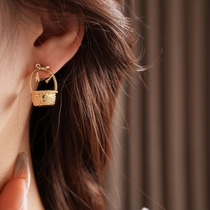 Detail of golden mini basket earring with a bow and woven texture on a model