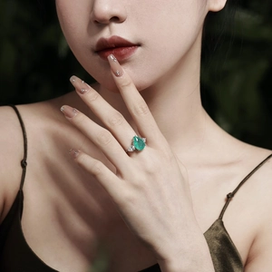 Detailed view of a pear-cut emerald silver ring with diamonds on a model hand