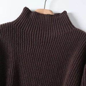 Detail of dark brown turtleneck sweater featuring thick ribbed knit texture on wooden hanger