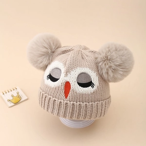Détail du bonnet en tricot pour bébé avec broderie hibou et deux pompons en fausse fourrure