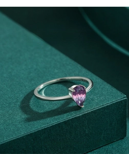 Close-up of a pear-cut purple gradient gemstone ring set in silver on a green surface