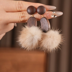 Detailed view of handmade wood earrings with beige pompom drop held by hand