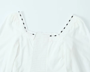 Détail de l'encolure carrée avec dentelle et ruban noir sur cette blouse en coton blanc