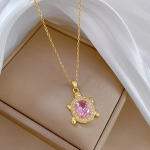 Close-up of gold turtle necklace with pink stone and white crystals in a jewelry box