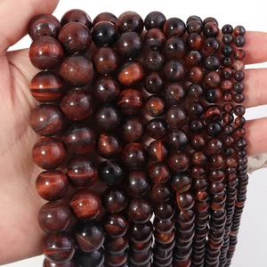 Close-up of natural red tiger eye stone beads in various sizes on a palm for DIY jewelry
