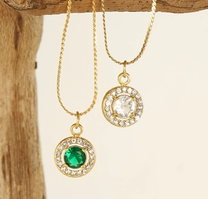 Detail of 18K gold-plated necklaces with green and white zircon pendants on wood