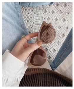 Detailed shot of oval frame sunglasses in matte beige finish held against denim background