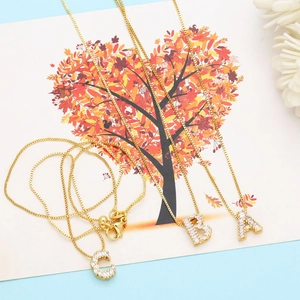 Detailed view of three gold box chain necklaces with iced out A, B, and C letter pendants