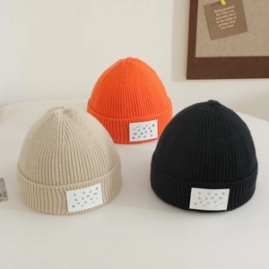 Detail of three ribbed knit beanies in orange, beige, and black with letter patches
