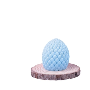 Blue 3D pinecone dragon egg candle on round wood slice with detailed scale texture