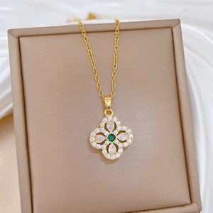 Golden clover pendant necklace with green gemstone and zircons on beige jewelry box