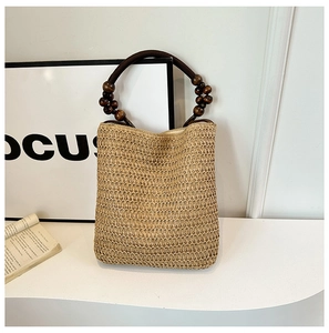 Detail of the woven straw bucket bag with dark brown circular handles and wooden beads